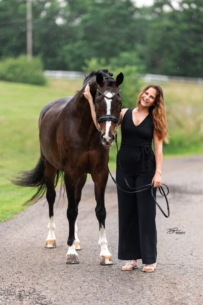 girl in black romper poses for an equine bond photoshoot with dark bay warmblood horse in the rain